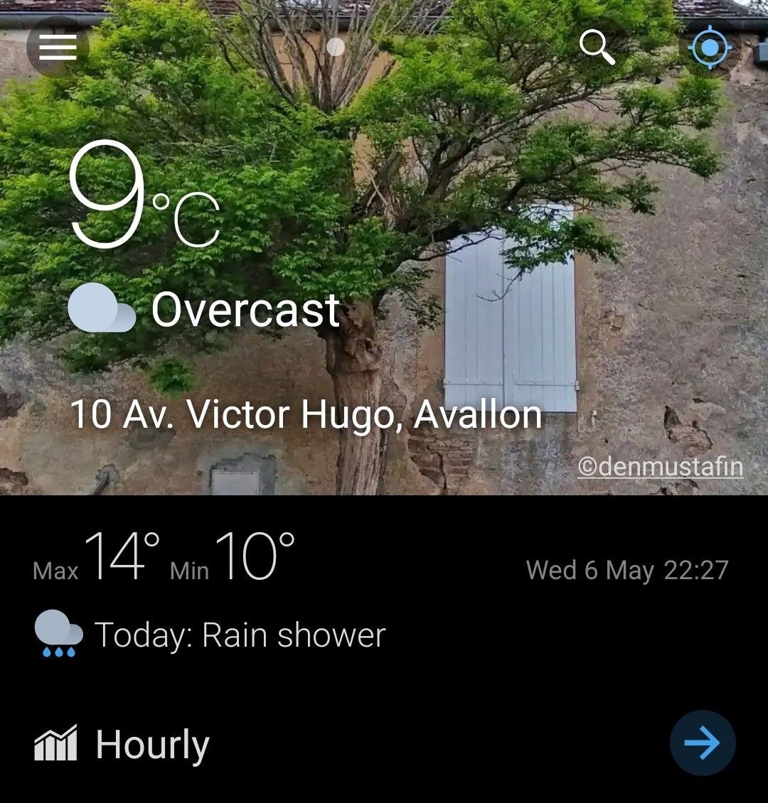 Weather application screenshot showing a photograph of a tree against an old wall in Avallon, with temperature, forecast and interface elements visible on screen.