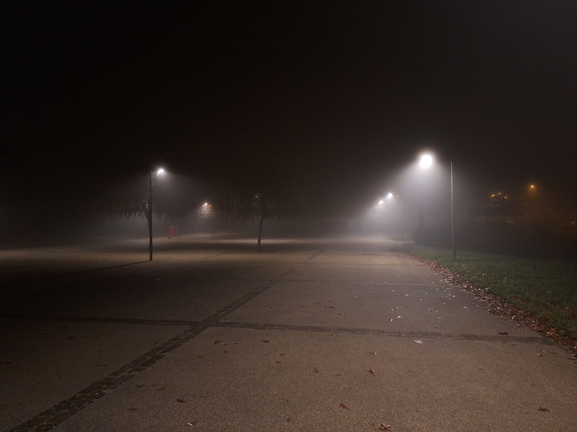 Empty public square at night in fog, illuminated by streetlights fading into darkness and mist.